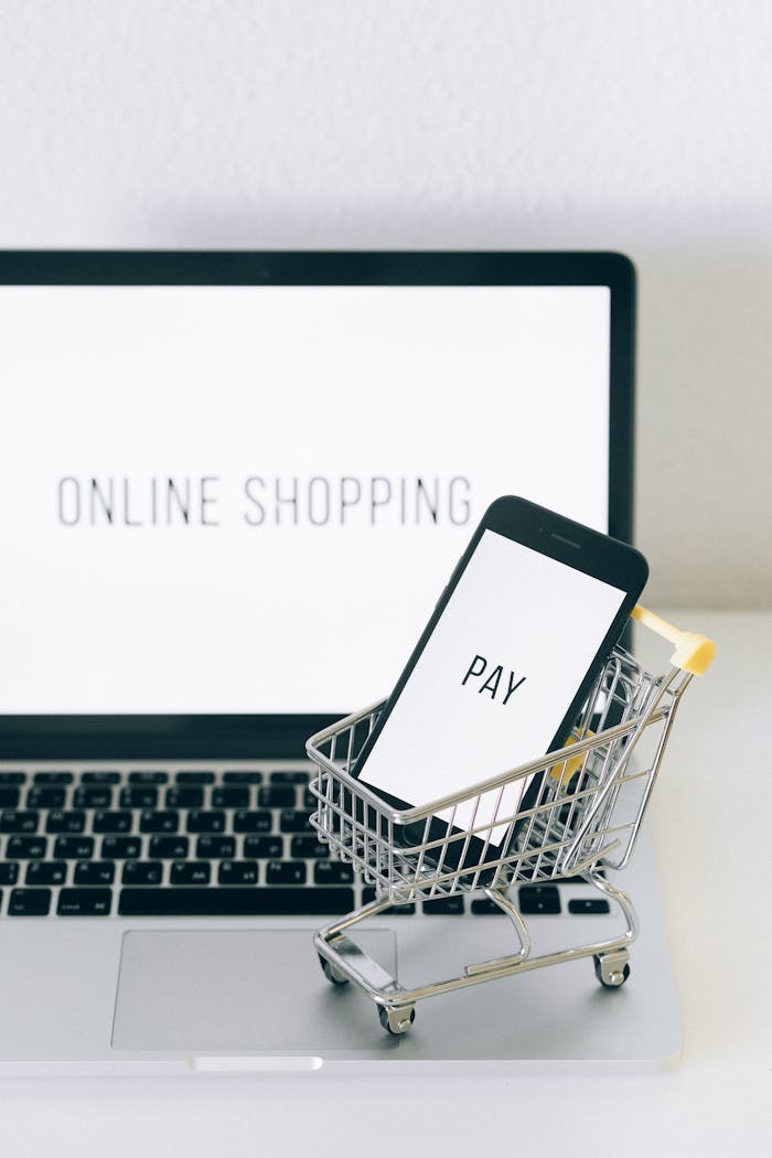 A smartphone in a miniature cart on a laptop symbolizes online shopping and digital payment.
